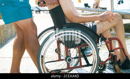 Homme handicapé à la plage nageant sur un fauteuil roulant avec aide sur une rampe d'accès. Banque D'Images