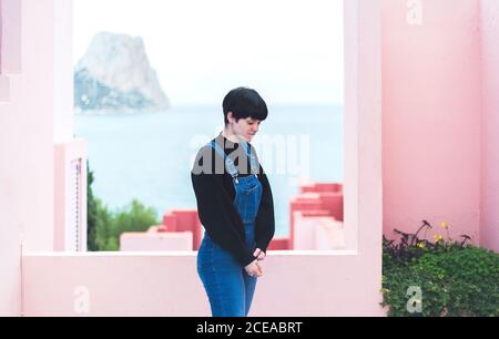Brunette jeune femme en chandail et dans l'ensemble avec les yeux fermés près des murs roses sur fond de mer Banque D'Images