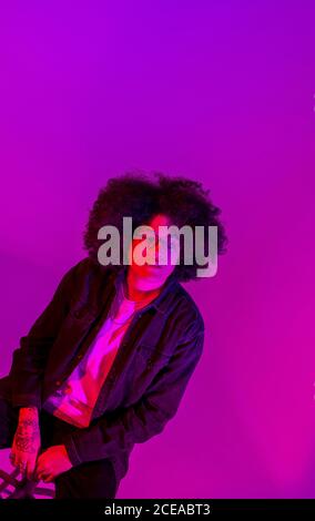 Homme en lunettes avec une coiffure afro assise sur une chaise au néon Banque D'Images