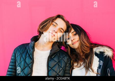 Homme heureux et femme attrayante en manteaux regardant l'appareil photo sur fond rose Banque D'Images