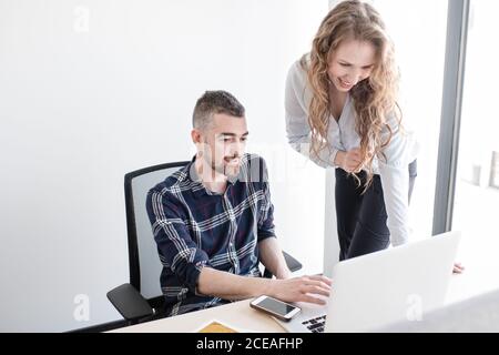 Femme et homme souriant au bureau regardant un ordinateur portable ensemble et travaillant en équipe à l'intérieur d'un bureau moderne Banque D'Images