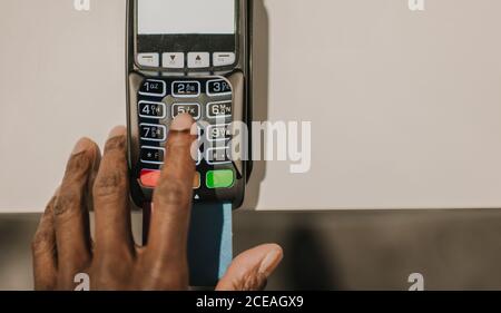 D'en haut de la main de l'homme afro-américain poussant touches sur le clavier du terminal de paiement moderne Banque D'Images