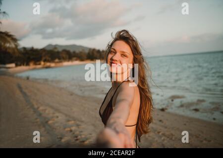 Jeune femme gaie debout sur la plage et tenant la main de photographe en Thaïlande. Banque D'Images