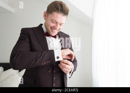 Vue d'en dessous du jeune homme souriant debout dans la chambre avec murs blancs et costume de mise Banque D'Images