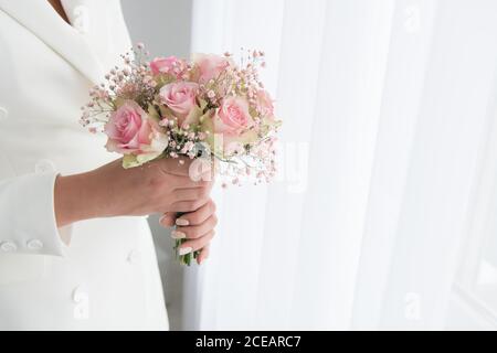 Photo sans visage de femme en costume élégant de mariée tenant un petit bouquet de roses Banque D'Images