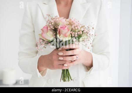 Photo sans visage de femme en costume élégant de mariée tenant un petit bouquet de roses Banque D'Images