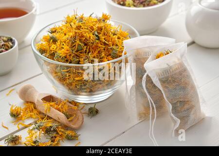 Bol de fleurs de marigold sèches, sachets de thé avec plantes Calendula sèches. Une tasse de thé et une bouilloire à thé sont situées sur une table en bois. Médecine alternative. Banque D'Images