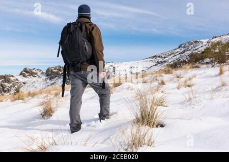 Jeune homme avec un sac à dos randonnée appréciant dans les montagnes enneigées lors d'une journée ensoleillée en hiver. Banque D'Images