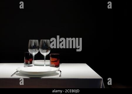 Table recouverte d'un chiffon blanc propre avec des verres vides et plaques isolées sur fond noir Banque D'Images