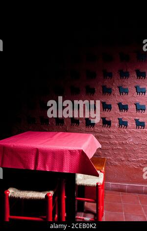 Table recouverte de tissu et chaises placées dans la pièce sombre avec mur en pierre rouge décoré de petites taureaux en papier noir Banque D'Images