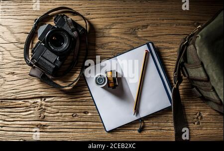 scène avec caméra analogique, bobines de film, bloc-notes avec stylo et sac photo sur une ancienne table en bois. Banque D'Images