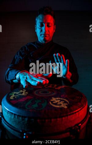 Jeune percussionniste pratiquant la technique avec le tam tam ou tambour, éclairage coloré en rouge et bleu. Banque D'Images