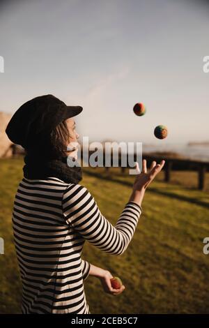 Dame élégante dans les balles de jonglage sur l'herbe près de la côte de la mer et du ciel avec Sun Banque D'Images