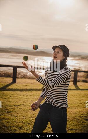 Dame élégante dans les balles de jonglage sur l'herbe près de la côte de la mer et du ciel avec Sun Banque D'Images