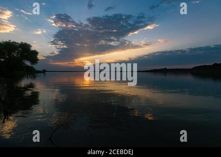 L'eau calme et vivivivivile d'un lac reflétant les nuages, la lumière du soleil et les arbres sur la rive tandis que le soleil se lève tôt le matin. Banque D'Images