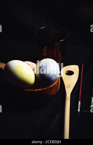 Petite brosse et support en bois placées près de bol avec les oeufs de Pâques peints sur fond noir Banque D'Images