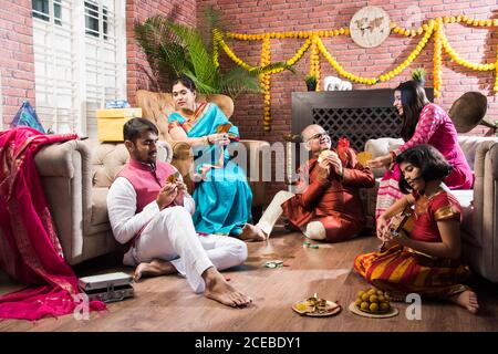 Happy Indian Family jouant à Teen patti ou à trois jeux de cartes le festival de diwali nuit en tenue traditionnelle à la maison Banque D'Images