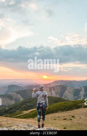 Vue arrière de la femme sportive à capuche tenant les bras élevés sur fond de majestueux paysage de montagnes au coucher du soleil Banque D'Images