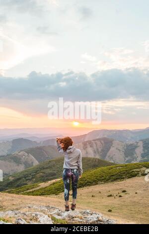 Vue arrière de la femme sportive à capuche tenant les bras élevés sur fond de majestueux paysage de montagnes au coucher du soleil Banque D'Images