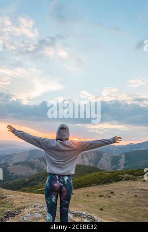 Vue arrière de la femme sportive à capuche tenant les bras élevés sur fond de majestueux paysage de montagnes au coucher du soleil Banque D'Images