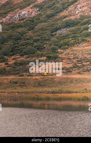 Personne en imperméable jaune allant sur la rive du lac près de wigam et colline à Isoba, Castille et Leon, Espagne Banque D'Images