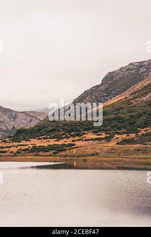 Personne en imperméable jaune allant sur la rive du lac près d'une montagne à Isoba, Castille et Leon, Espagne Banque D'Images