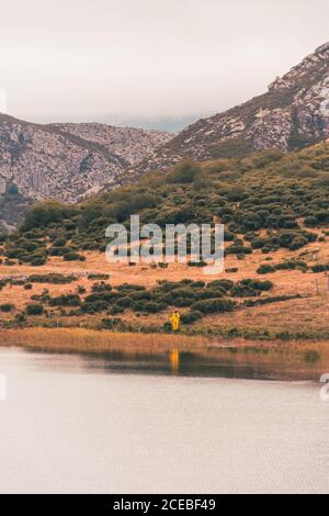 Personne en imperméable jaune allant sur la rive du lac près d'une montagne à Isoba, Castille et Leon, Espagne Banque D'Images