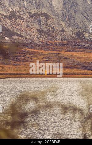 Personne en imperméable jaune allant sur la rive du lac près d'une montagne à Isoba, Castille et Leon, Espagne Banque D'Images