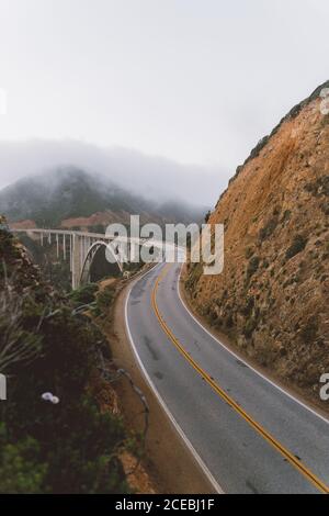 Route asphaltée étroite et magnifique pont situé près de la pente de montagne le jour de brouillard à Big sur, Californie Banque D'Images