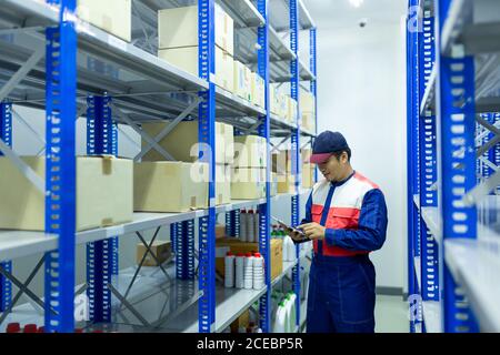 Travailleur asiatique dans un entrepôt de pièces de rechange automobile vérifiant les produits Banque D'Images