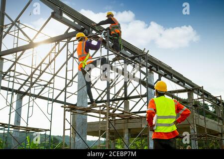 Le contrôle des ouvriers de la construction en Asie dans la construction de structures de toit et les travailleurs portent des équipements de hauteur de sécurité pour installer le toit. Dispositif antichute de Banque D'Images