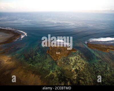 Vue aérienne sur une vaste surface d'eau de mer avec pittoresque peu profonde baie et petite île avec des bâtiments sur elle au soleil jour Banque D'Images