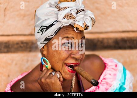 CUBA - 14 septembre 2017 : vue rapprochée de la jeune femme afro-cubaine senior avec une grande fleur rouge sur la bruyère tenant le cigare dans la bouche et regardant l'appareil photo sur un arrière-plan flou Banque D'Images