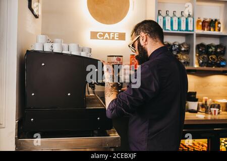 Vue latérale de l'homme barbu tatoué qui travaille comme barista café-restaurant et cafetière Banque D'Images