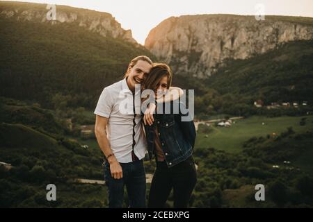 Couple mignon qui épouse et durcir les fronts en se tenant debout sur l'arrière-plan de belle vallée et montagnes Banque D'Images