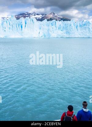 Vue arrière de deux touristes admirant le calme de la mer froide et spectaculaire falaise de glace par jour nuageux en Argentine Banque D'Images