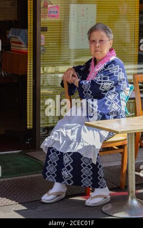 Japon - Mai 10 2013: Femme asiatique senior dans un kimono regardant la caméra tout en étant assis à une table de café le jour ensoleillé sur la rue de la ville Banque D'Images
