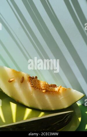 Demi-peau de crapaud de Melon coupée en coupe. Thème estival coloré. Sur fond bleu et vert, ombres des feuilles de palmier Banque D'Images