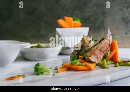 poisson au scorpion grillé avec purée de pois et bâtonnets de carottes, sur une assiette en marbre Banque D'Images