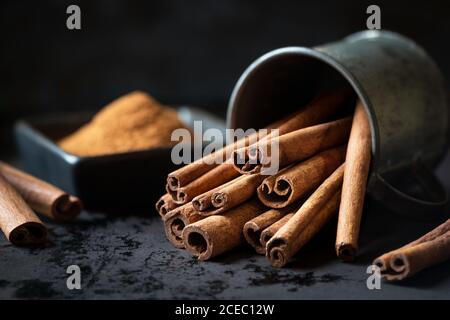 Bouquet de bâtons de cannelle aromatiques couchés dans une tasse en métal plan d'examen sombre Banque D'Images