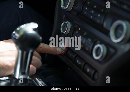 Récolte en gros plan de l'homme qui appuie sur le bouton de démarrage du moteur sur le tableau de bord d'une voiture de luxe moderne Banque D'Images
