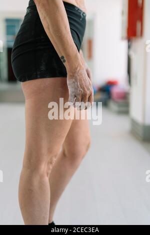 Vue latérale d'une athlète féminine anonyme avec les mains couvertes craie debout dans la salle de gym pendant l'entraînement Banque D'Images