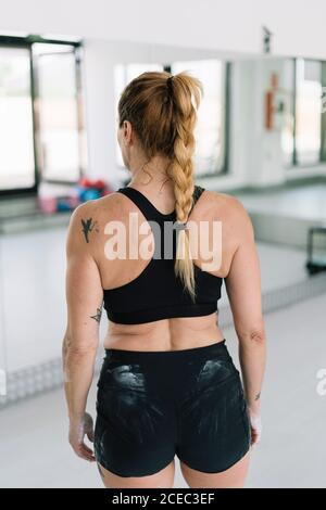 vue arrière d'une athlète féminine anonyme avec les mains recouvertes de craie debout dans la salle de gym pendant l'entraînement Banque D'Images