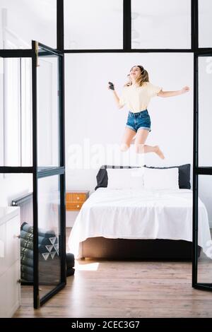 Femme excitée avec le téléphone sautant sur le lit Banque D'Images