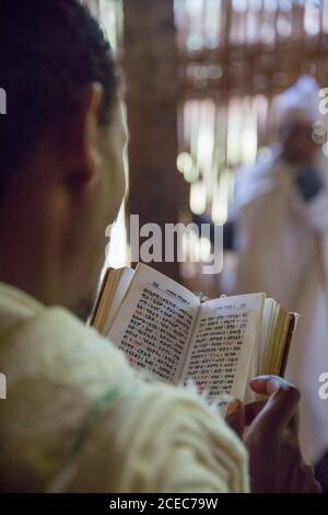 Rognez la vue arrière du parishioner anonyme lisant le livre de prière sur arrière-plan de l'église flou Banque D'Images