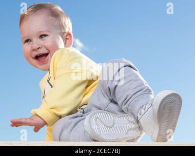 Joyeux petit garçon assis dans des vêtements décontractés et s'amusant sur fond bleu. Banque D'Images