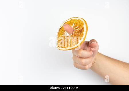 Vue d'une main avec l'index tenant un tranche d'orange séchée à travers le trou sur fond blanc Banque D'Images