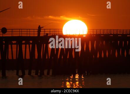 Un homme pêchant dans la lumière du matin tandis que le soleil se lève au-dessus de Blyth Pier dans Northumberland le premier jour de l'automne météorologique. Banque D'Images