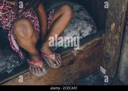 Récolte de dessus de la pauvre petite fille assis dessus matelas abîmé en mauvais état sur un lit en bois Banque D'Images