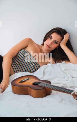 Jeune femme brune couchée au lit avec guitare Banque D'Images